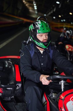 Spor giyim ve kask süren adam kapalı alanda karting yapmak için spor araba kullanıyor, hobi olarak.