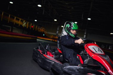 Kasklı ve spor giyimli bir yarışçı kapalı devre üzerinde go kart, adrenalin konsepti
