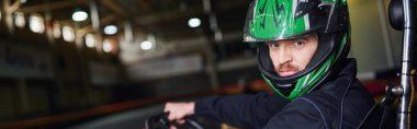 Miğferli ve spor giyimli bir adamın portresi. Kapalı devre üzerinde go kart, adrenalin pankartı.