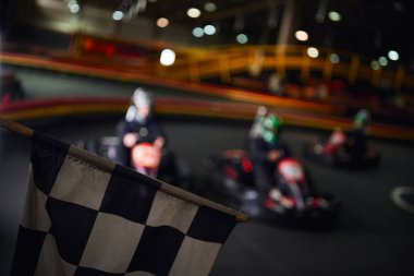Bulanık arka planda sürücüler olan siyah beyaz yarış bayrağı, go kart konsepti