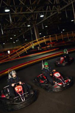 group of multiethnic people driving go kart on indoor circuit, speed racing and competition clipart