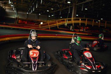 focused multicultural go cart racers driving on indoor circuit, speed racing and motorsport clipart