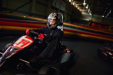 focused speed racer in helmet driving go kart car on indoor circuit, motorsport competition concept clipart