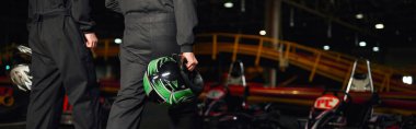 Go kart sürücülerinin spor kıyafetleri içinde gezerken, miğfer ve afiş tutarken çekilmiş görüntüsü.