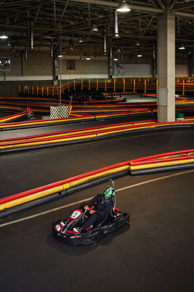 Африканский американец в шлеме в картинге на крытой картинговой дорожке, активное хобби