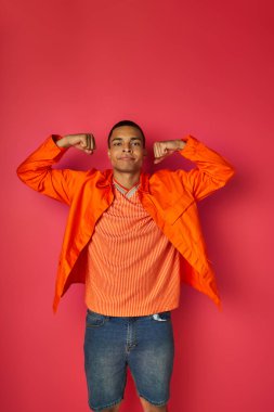 confident african american man in orange shirt demonstrating strength on red background clipart