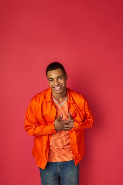 Mutlu Afro-Amerikan adam göğsüne dokunuyor, kameraya gülümsüyor kırmızı, minnet dolu jest, turuncu gömlek