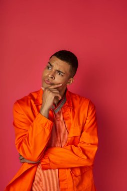 Düşüncelere dalmış turuncu gömlekli Afro-Amerikan adam göğsüne dokunuyor ve yüzünü kızıla çeviriyor.