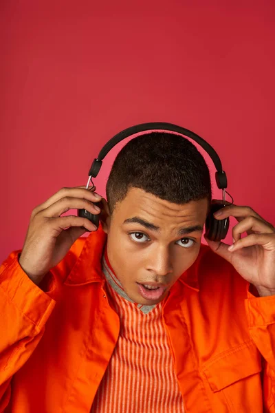 赤い背景でワイヤレスヘッドフォンで音楽を聞いているスタイリッシュなアフリカ系アメリカ人男性 — ストック写真