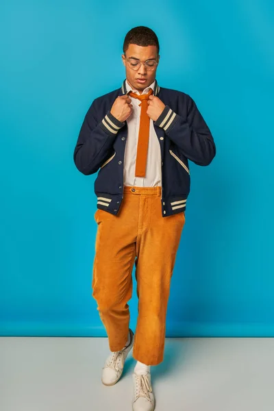 青い背景に立っているジャケット ネクタイ オレンジ色のパンツの若いアフリカ系アメリカ人学生 — ストック写真