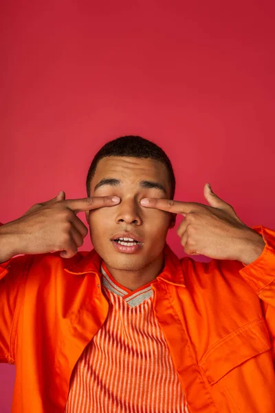 Позитивный Африканский Американец Оранжевой Рубашке Затмевает Глаза Пальцами Красном Фоне — стоковое фото