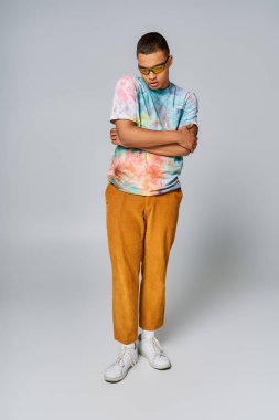 trendy african american man with folded hands on grey, tie-dye t-shirt, orange pants, sunglasses clipart