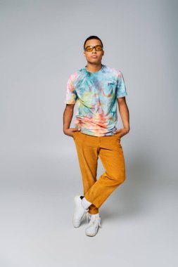 trendy african american man with hands in pockets on grey, orange pants, sunglasses, tie-dye t-shirt clipart