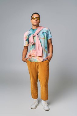 Kendine güvenen Afro-Amerikan erkeği, turuncu pantolon, güneş gözlüğü, kravat boyası tişört, elleri cebinde, gri