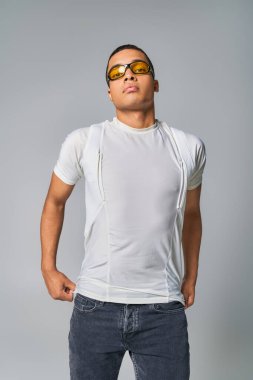 Modern moda, Afro-Amerikan tişörtlü, kot pantolonlu ve güneş gözlüklü adam gri kameraya bakıyor.