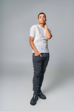 Tişört ve kot pantolonlu modern Afro-Amerikan vatandaşı, el ele verip gri renkli kameraya bakıyor.