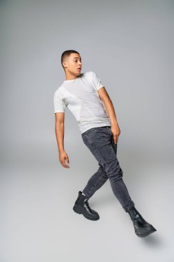 Sıradan moda, genç Afro-Amerikan tişörtlü ve kot pantolonlu, tam boy gri poz veriyor.