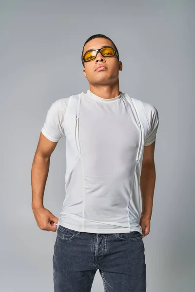 stock image modern fashion, african american guy in t-shirt, jeans and sunglasses looking at camera on grey