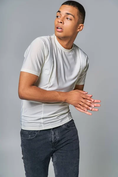 modern fashion, young african american in t-shirt and jeans, looking away on grey