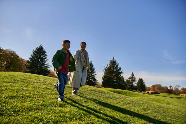 солнечный осенний день, веселая африканская женщина, бегущая вместе с сыном в парке, веселая
