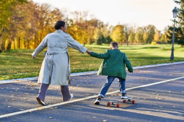 boy in outerwear riding penny board and holding hands with mother, african american,  autumn leaves clipart