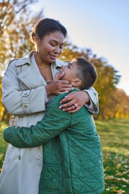 motherly love, joy, african american woman hugging with son, standing near golden leaves, autumn clipart