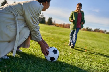 Futbolla mutlu bir Afrikalı Amerikalı kadın, oğluna bakan bir anne, bulanık bir arka plan, yeşil bir alan.