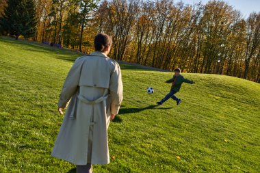 Yeşil tarlada, futbol, sonbahar, sonbahar, sonbahar, sonbaharda annesinin yanında futbol oynayan tatlı Afrikalı Amerikalı çocuk.