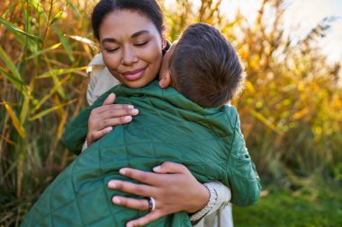 happiness, motherly love, african american mother hugging son in autumnal outerwear, fall season clipart