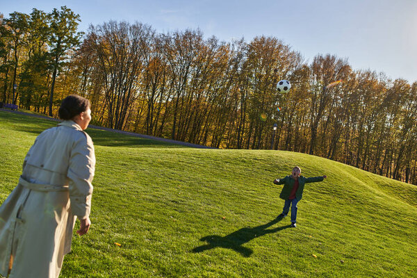amazed african american boy playing football with mother on green field, screaming, running, soccer