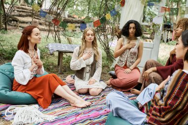 Çok ırklı ve stil sahibi kadınlar Boho tarzı giyinmiş, inziva merkezinde birlikte meditasyon yapıyorlar.