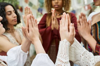 Çok ırklı kadınlar dua ederken dışarıda, dinlenme merkezinde vakit geçirirken el hareketi yapıyorlar.