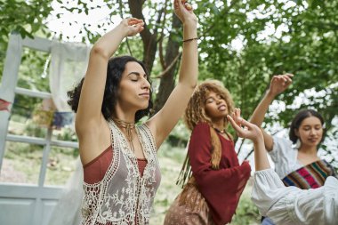 Boho kıyafetleri içinde şık, çok kültürlü bir kadın. İnziva merkezinde gözleri kapalı, arkadaşlarının yanında dans ediyor.