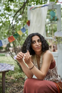 Gülümseyen, çok kültürlü bir kadın. Boho kıyafetli. İnziva merkezinde oturuyor ve zaman geçiriyor.