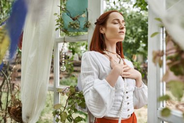 stylish redhead woman in boho outfit standing in patio outdoors in retreat center clipart