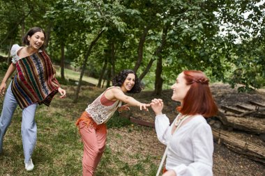 Boho kıyafetleri içinde neşeli çoklu etnik kadınlar inziva merkezindeki çayır üzerinde eğleniyorlar.