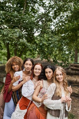 joyful multiethnic group of women looking at camera and hugging in retreat center clipart