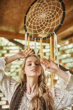 portrait of young boho style woman posing near dream catcher in cottage of retreat center clipart