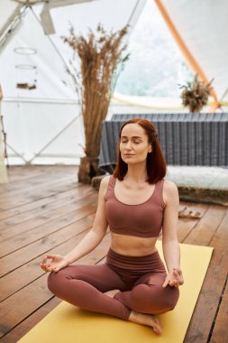 Spor kıyafetli kadın Lotus 'ta meditasyon yapıyor. Gözleri kapalı poz veriyor. Geri çekiliş merkezinde, sükunet içinde.