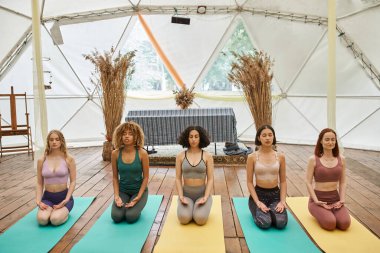 Çok ırklı kadınlar kapalı gözlerle, spor kıyafetleriyle, şimşek gibi meditasyon yapıyorlar.