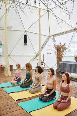 Spor giysilerinde çok ırklı kız arkadaşlar şimşek şeklinde meditasyon yapıyorlar modern geri çekilme merkezinde poz veriyorlar.