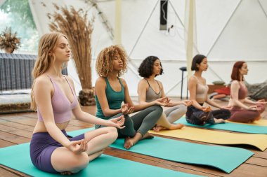Spor giyim sektöründe çok ırklı kız arkadaşlar Lotus 'ta meditasyon yaparken gözleri kapalı geri çekiliyorlar.