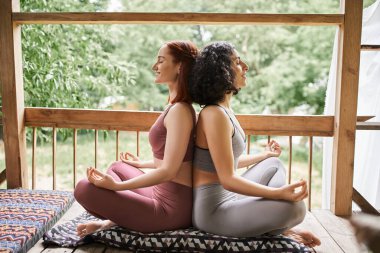 Spor kıyafetleri içinde kaygısız kız arkadaşlar Lotus 'ta meditasyon yapıyorlar. Kapalı gözlerle, dinlenme merkeziyle, terasta.