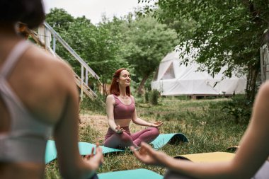 Nilüfer çiçeğinde meditasyon yapan kaygısız kadın açık hava inziva merkezinde bulanık kız arkadaşlarının yanında poz veriyor.