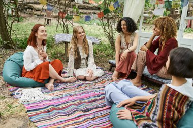 Parkta renkli battaniyeyle konuşan mutlu çoklu etnik kız arkadaşlar, kadınlar geri çekilme kavramı