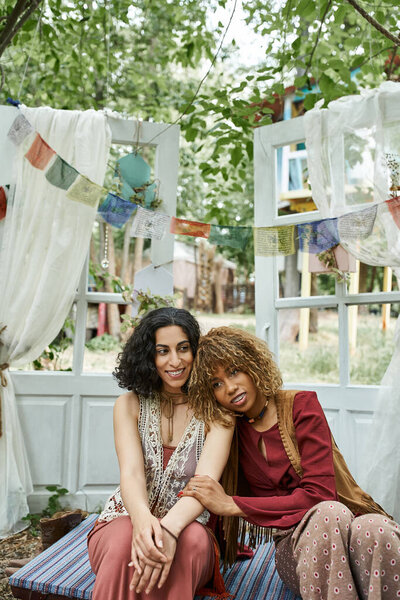 smiling african american woman hugging multiracial friend in boho outfit in retreat center