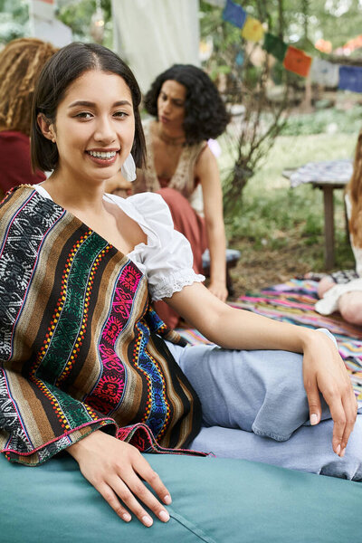 stylish and smiling woman looking at camera near blurred multiethnic women in retreat center