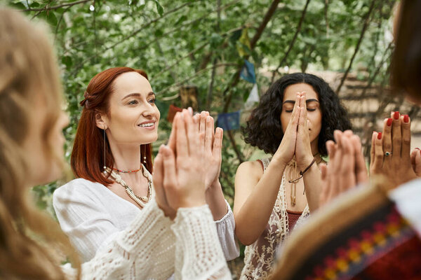 smiling redhead woman meditating with multiethnic friends outdoors in retreat center