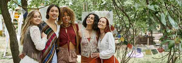 smiling interracial girlfriends looking at camera outdoors in retreat center, banner
