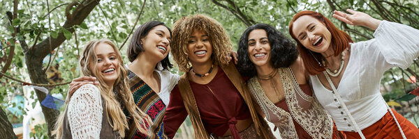 cheerful interracial women in boho styled clothes looking at camera in retreat center, banner